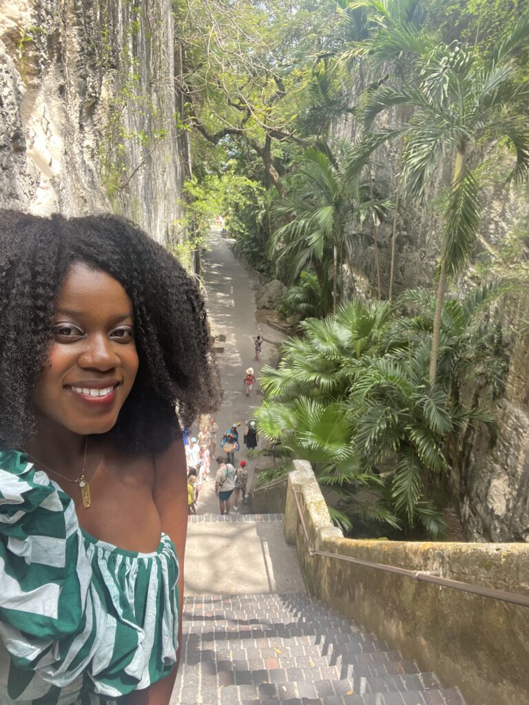 Black woman with afro and green and white stripped dress smiling in front of outdoors regal looking staircase