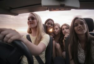 5 young women are driving in a convertible car while on a girls trip